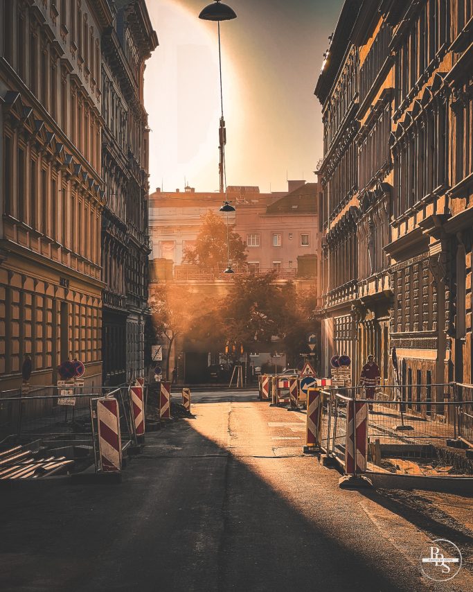 Stadtstraße mit Baustellenabsperrungen bei Sonnenuntergang, warmes Licht.
