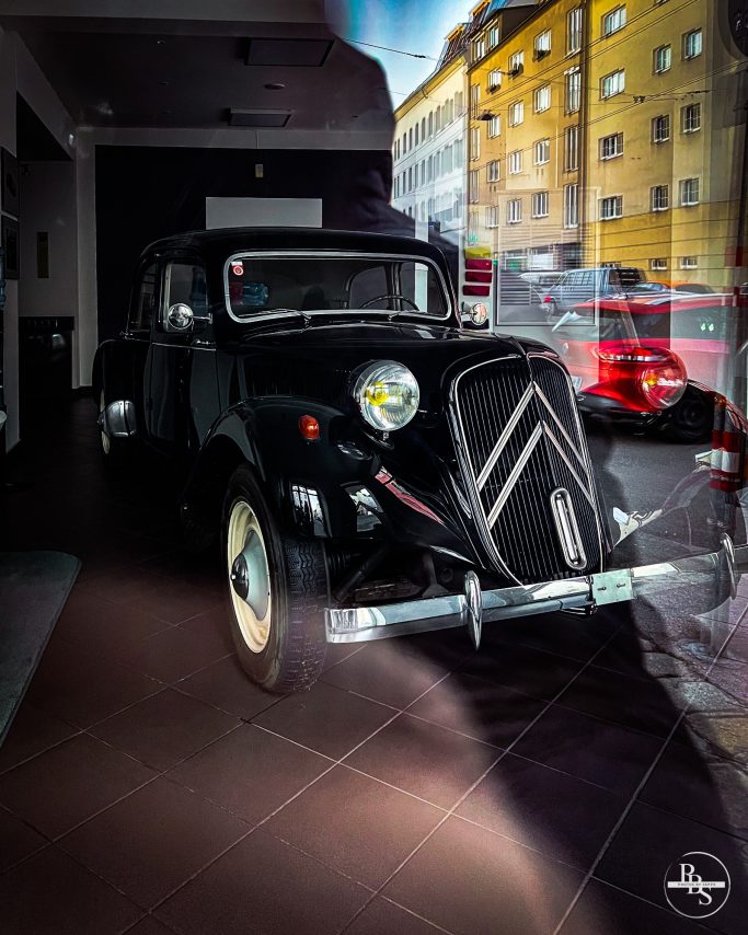 Schwarzes klassisches Auto in einem Showroom, mit moderner Architektur im Hintergrund.