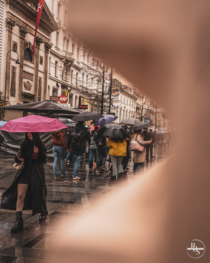 Regentropfen auf der Straße, Menschen mit Regenschirmen und nassen Bürgersteigen.