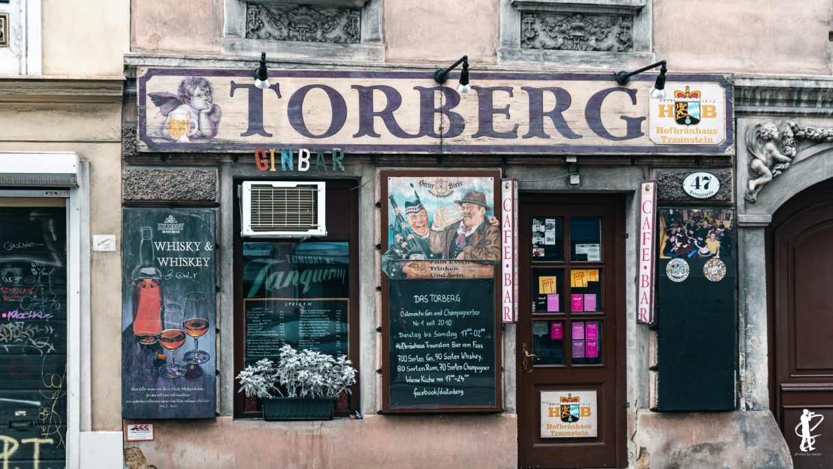 Schild des Lokals "Torberg" mit Speisenangebot und bunten Tafeln.