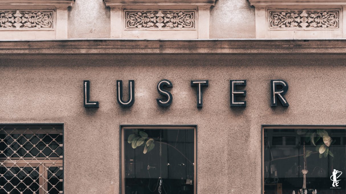 Schriftzug „LUSTER“ an einer Wand mit dekorativen Details.