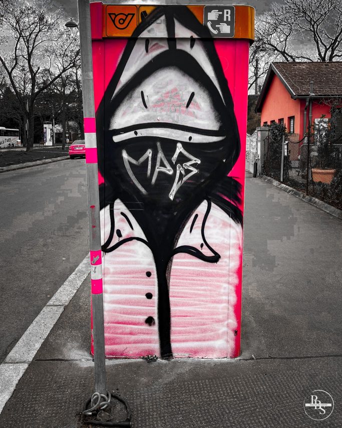 Graffiti eines stilisierten Gesichts in Schwarz und Pink auf einem Stromkasten.