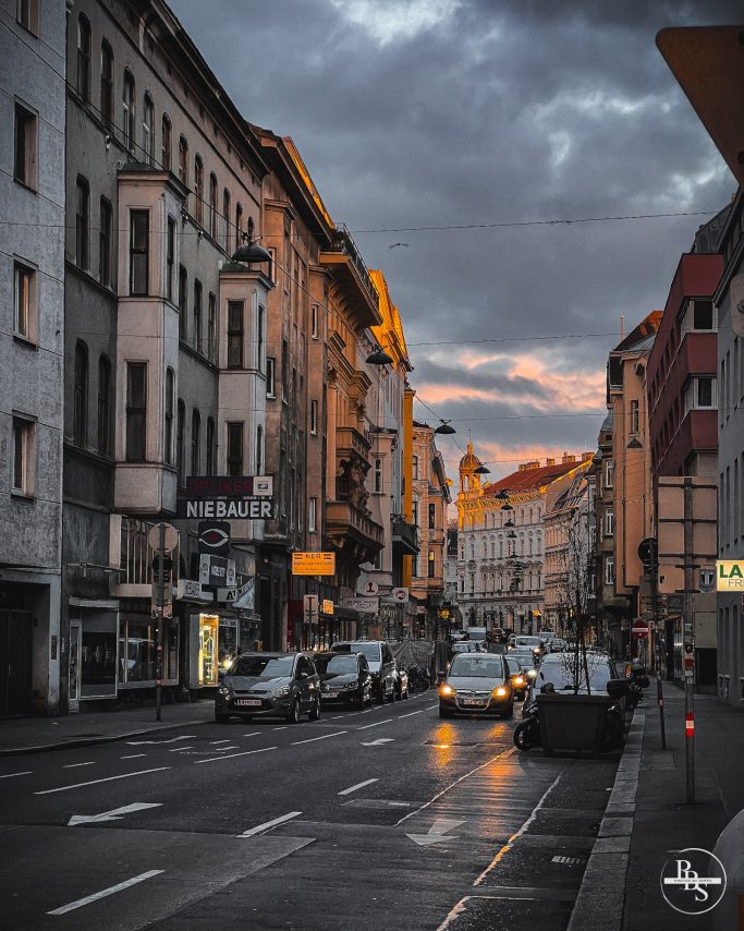 Straße in einer Stadt bei Sonnenuntergang, mit Autos und historischen Gebäuden.