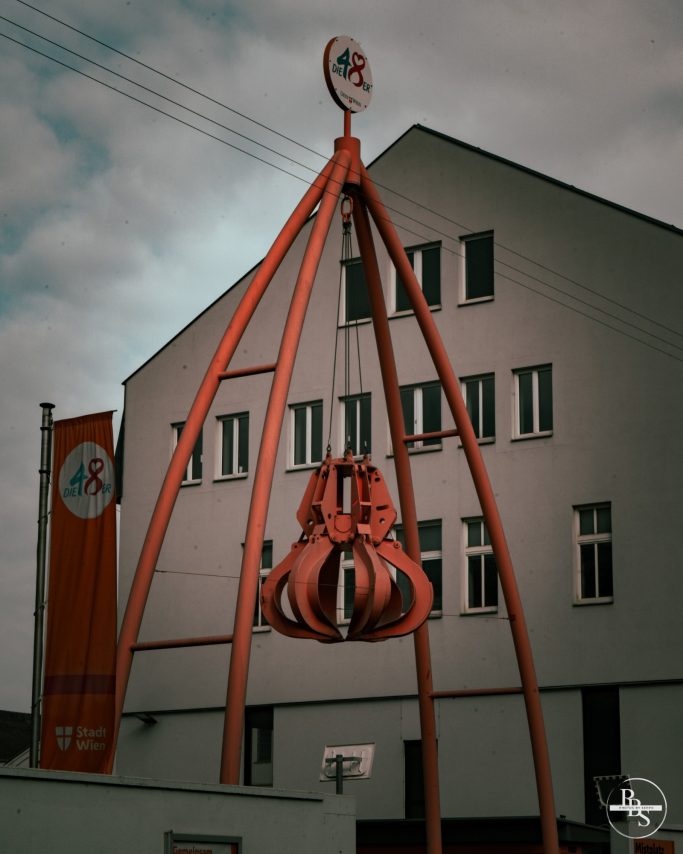 Ein rotes, skulpturales Objekt steht vor einem modernen Gebäude mit Fenstern.