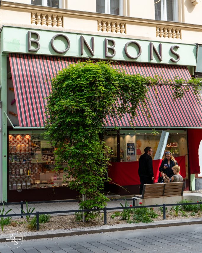 Süßwarenladen "Bonbons" mit einer Begrünung und Personen davor.